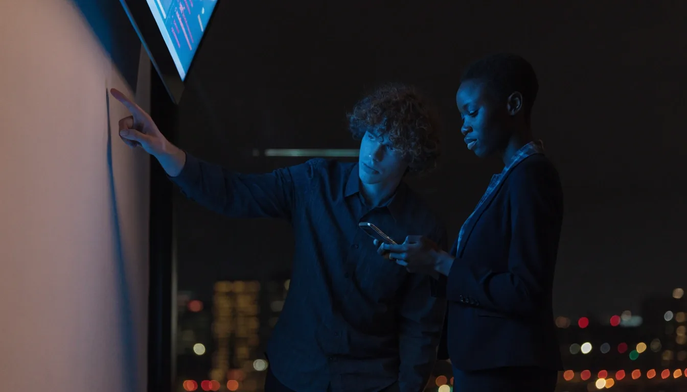 Developers watching an evening deployment in a dim Seattle office with city lights outside
